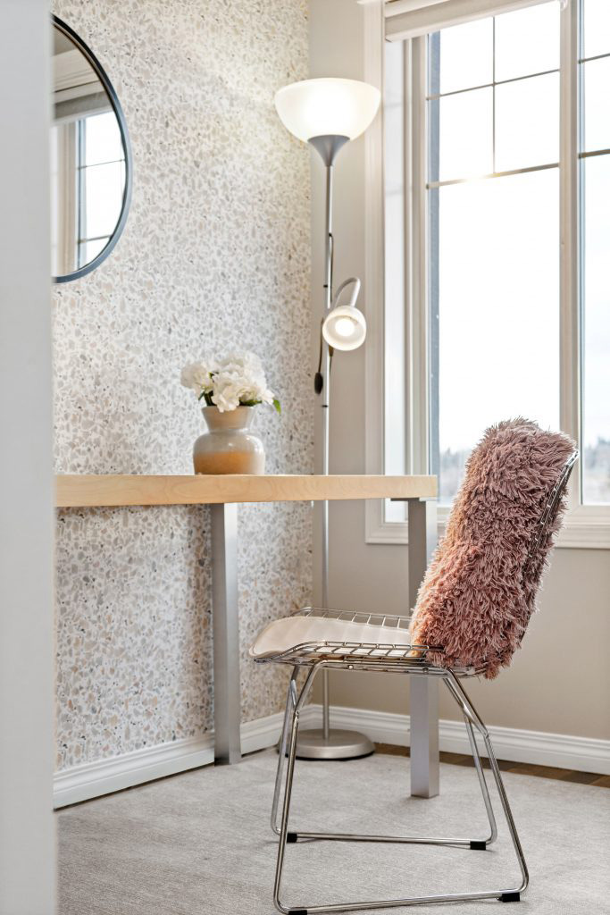 an airbnb office space with light wooden desk, peach and grey vase with florals and a chair with fluffy pink pillow