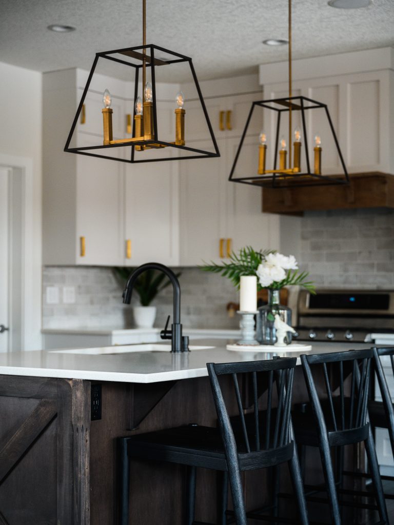 a modern farmhouse designed kitchen island with brass and black hanging lights and barn style island ends