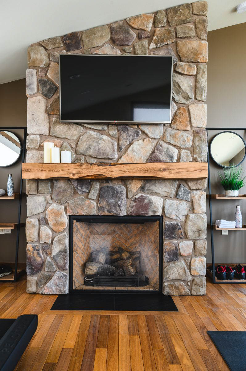 a tall stone fireplace, with a unique carved wood shelf, styled with candles to maintain a simple look as the room is busy