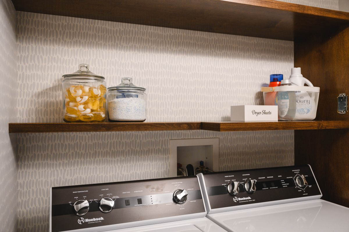 floating shelves above the washer and dryer, topped off with a bin and glass containers