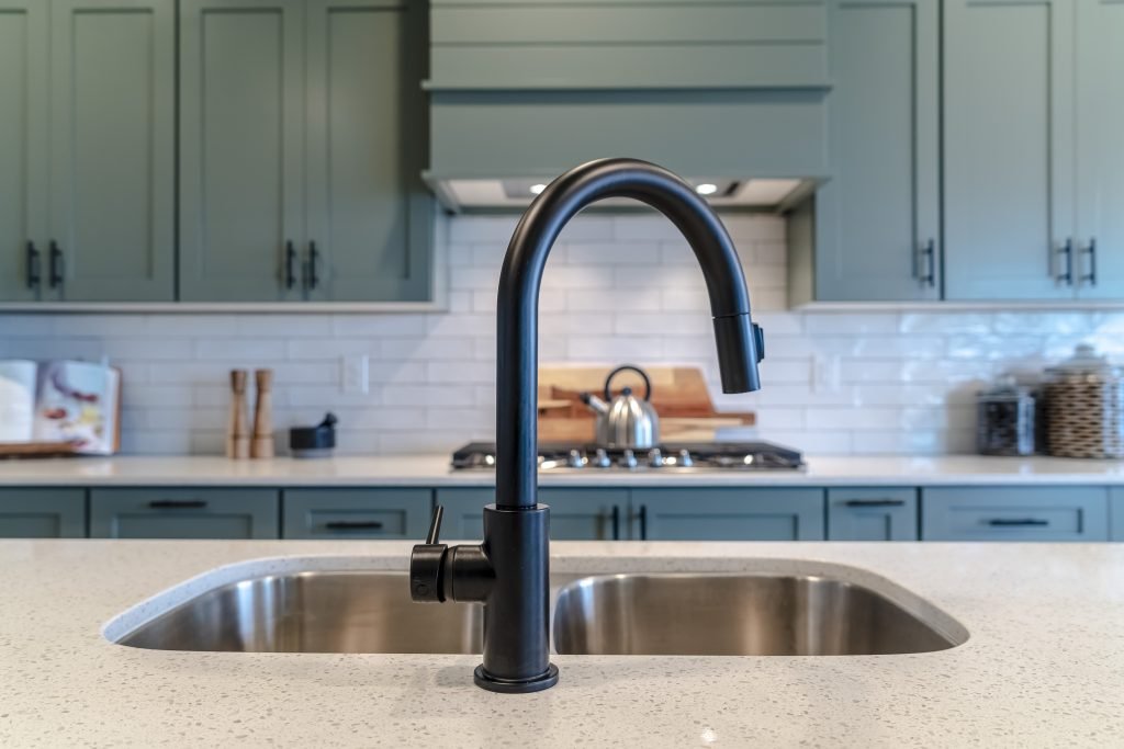 Double bowl kitchen island sink with black faucet against cooktop and cabinets. The double basin undermount sink is made of stainless steel.
