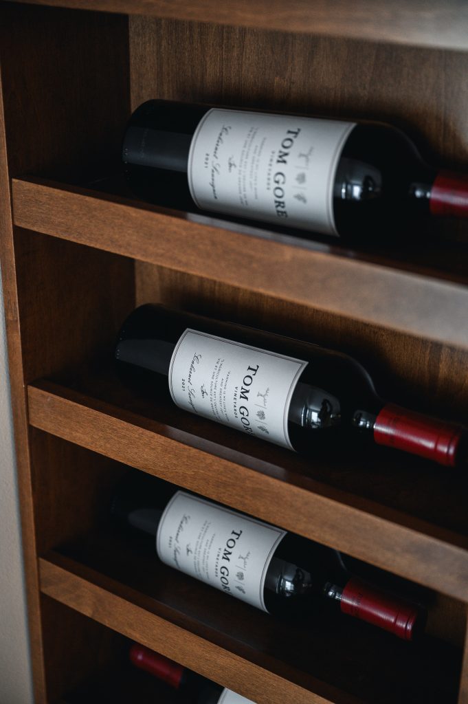Tuscany Estate Interior Decorating Wine Tasting Room Wine Shelf Detail Unshelf Design. Open wood shelving with red wine on display.