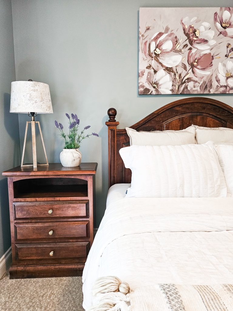 Transitional Inglewood Home Home Staging Primary Bedroom Wood Headboard Detail Unshelf Design. Pink floral artwork above a queen size bed with modern decor.