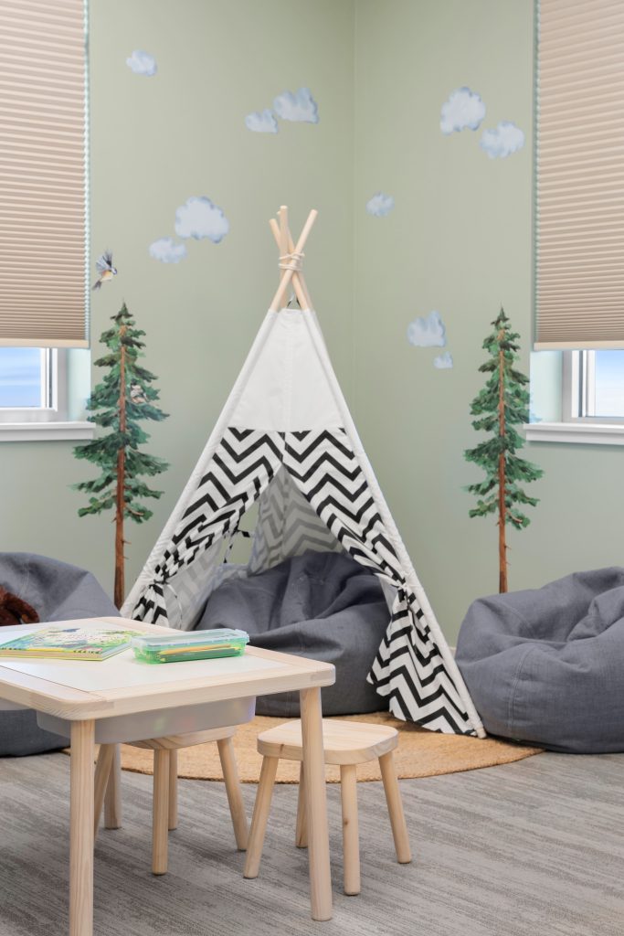 Psychology clinic commercial decorating jungle playroom childrens teepee tent Unshelf Design. Soft green jungle playroom with children's teepee tent among grey bean bag chairs.
