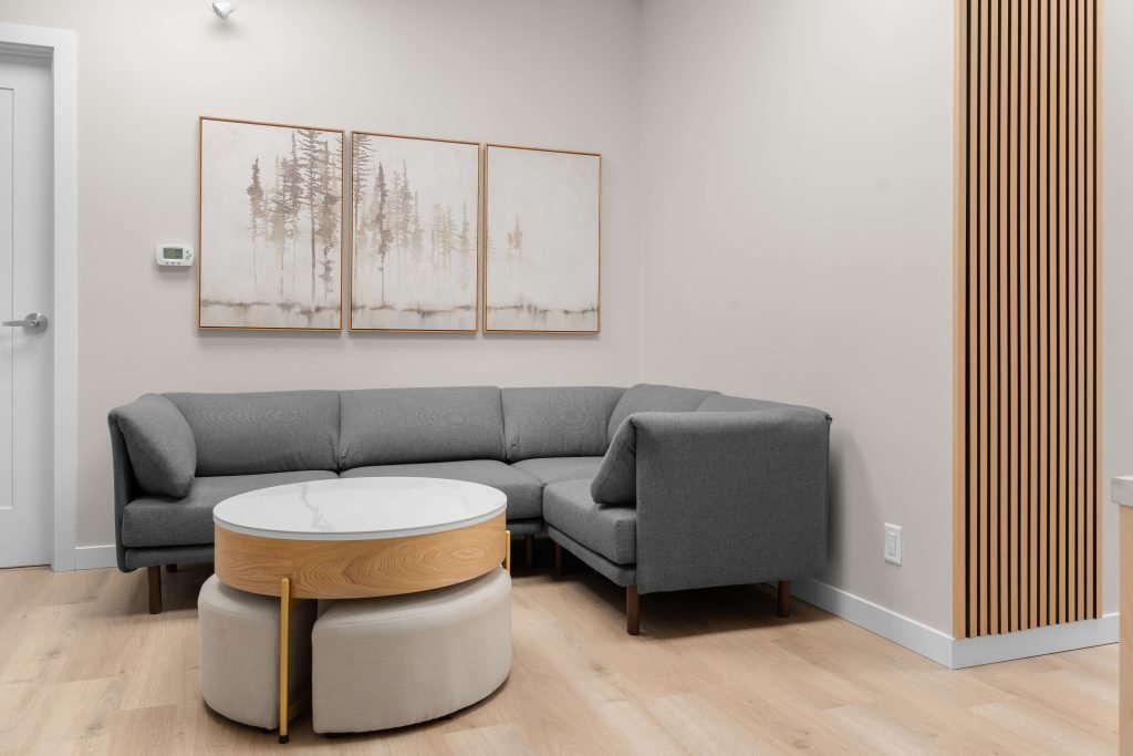Psychology clinic commercial decorating waiting room grey couch Unshelf Design. Modern grey couch behind coffee table with built in stools.