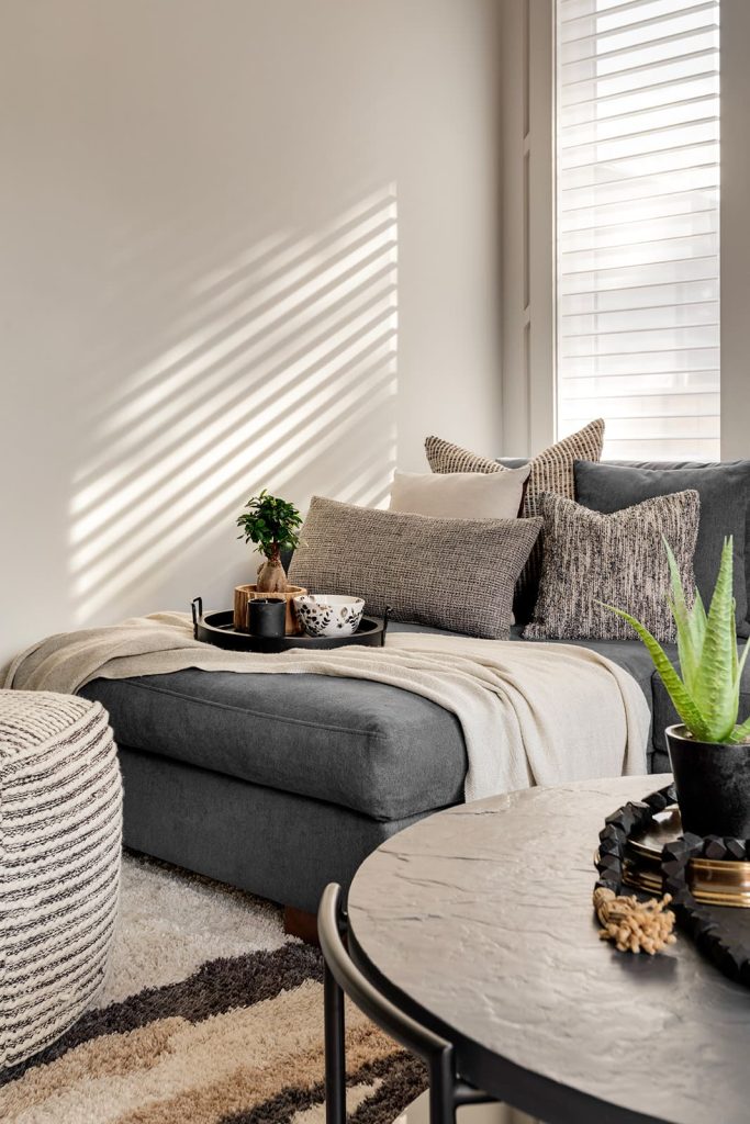 Decor sits on end of grey couch, on top of cream throw blanket. Modern mountain design interior furnishing & decorating moody living room design Unshelf Design