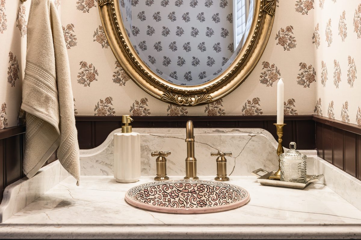 Close-up of a brass faucet over a patterned sink with marble countertop in a Victorian-style powder room.
