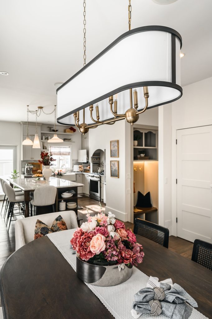 Open-concept dining area with a dark oval table, cane chairs, and a long oval pendant light with a view into the kitchen beyond.