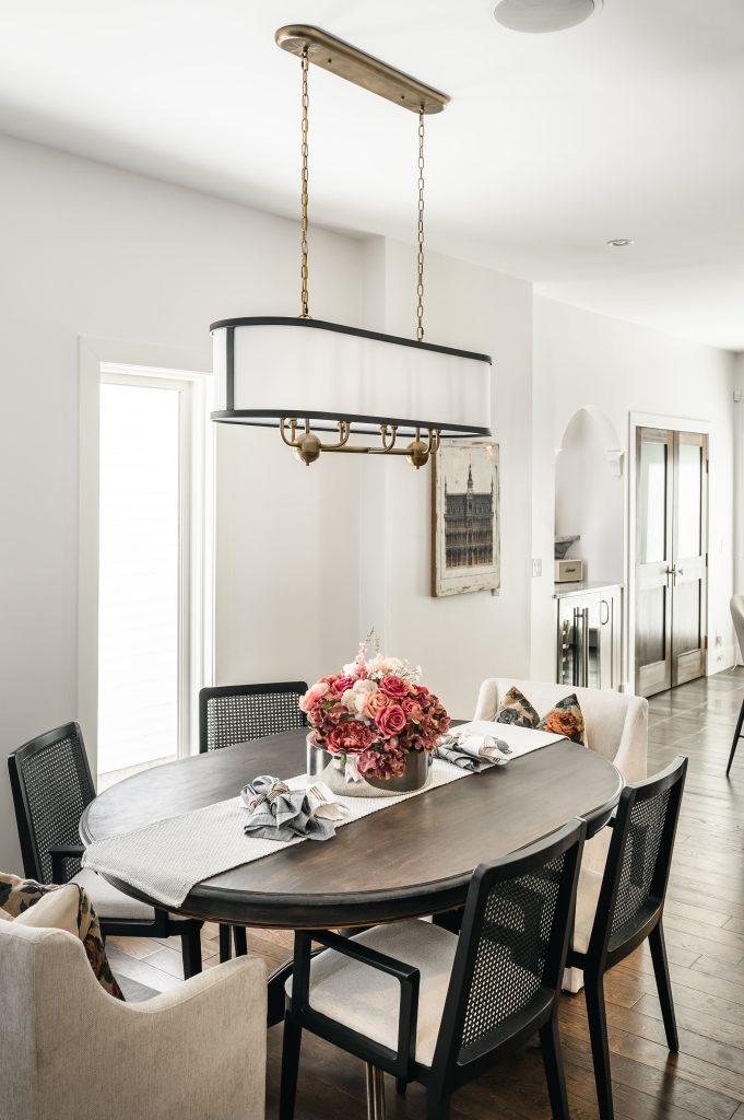Elegant light shade pendant with brass detailing hanging above a dark oval dining table with a pink floral centerpiece.
