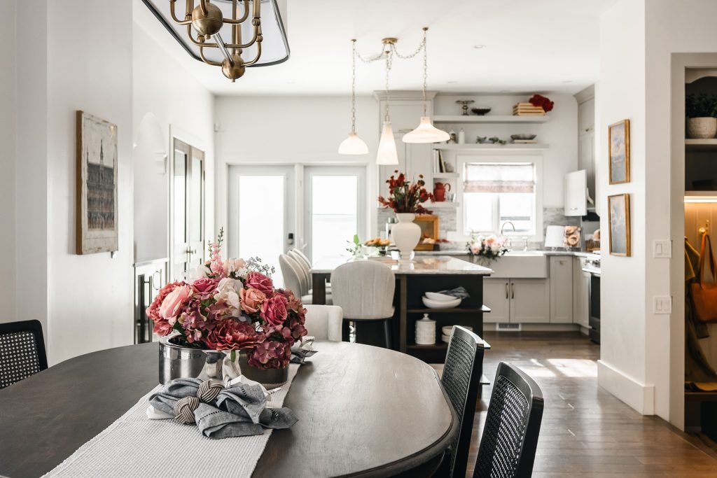 Open-concept dining room with a dark oval dining table and chairs flowing into the Victorian-inspired kitchen beyond.