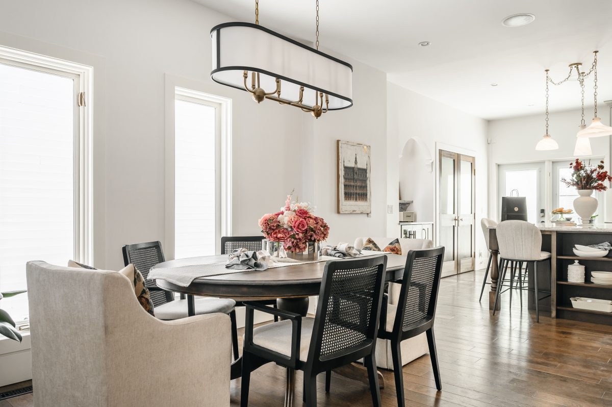 Dining room with a dark oval table, cane-back chairs, linen crown chairs, and a lush floral centerpiece under an oval pendant.