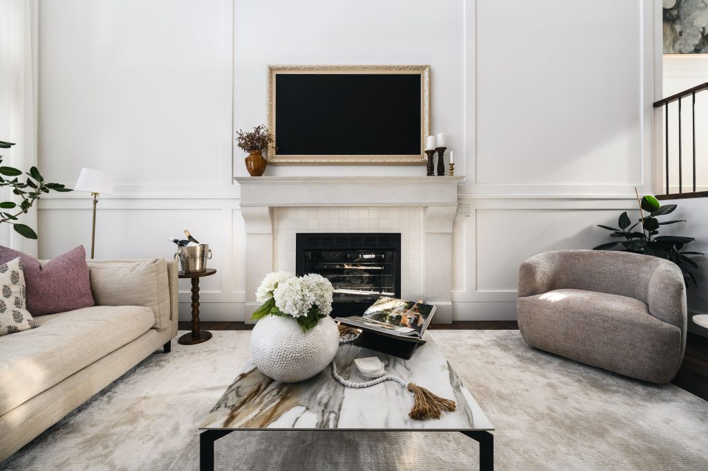 Tile fireplace, mantle styled with a gold-framed TV, terracotta vase, and pillar candles in a panelled English country living room.