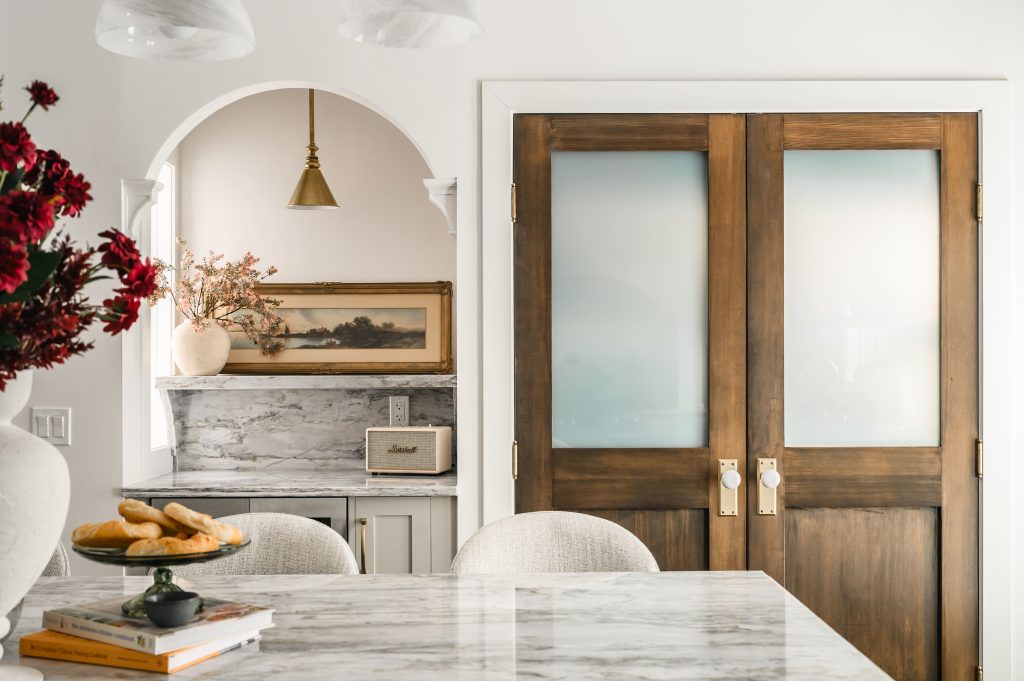 Kitchen with a large marble island and bar stools beside wood-framed frosted glass French doors.