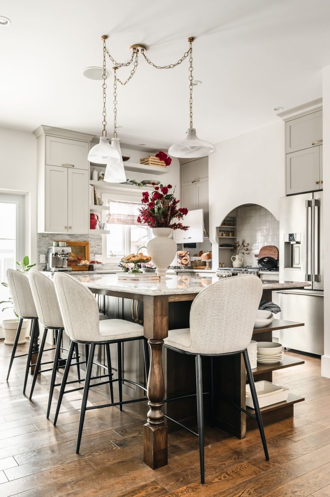 Marble-topped kitchen island with cream upholstered counter stools in an English country kitchen with shaker cabinets.
