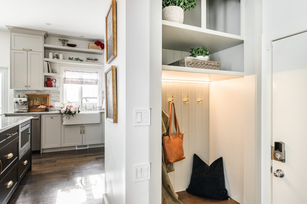 Connecting hallway showing a farmhouse-style kitchen on one side and a built-in mudroom with hooks and shelving on the other.