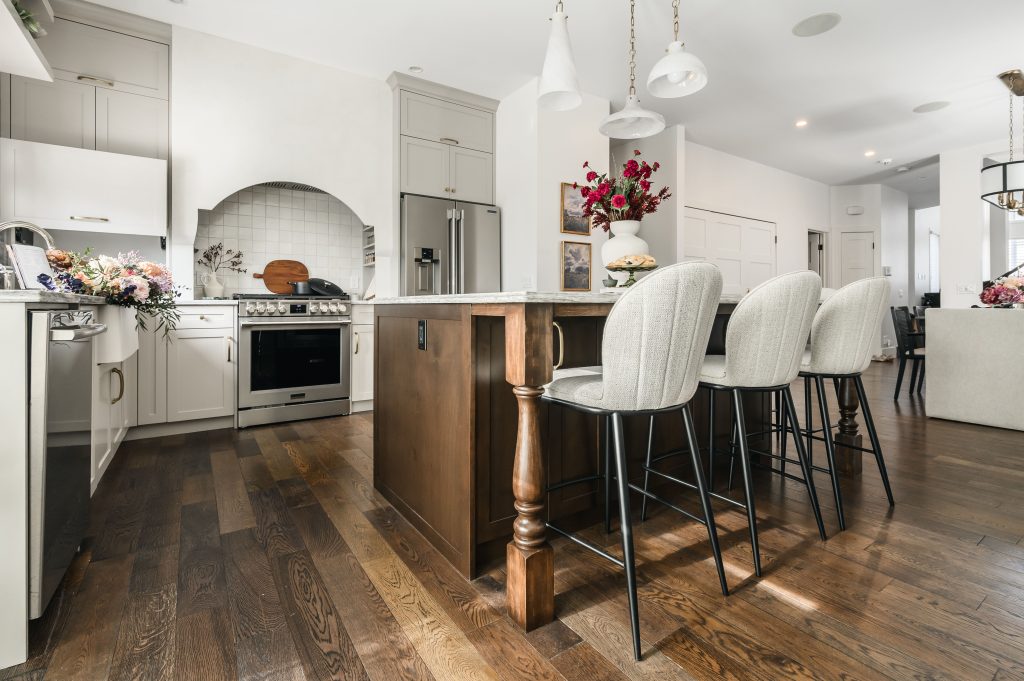 Open-plan kitchen with a marble island, light bar stools, and a stainless steel range visible from the dining and living areas.