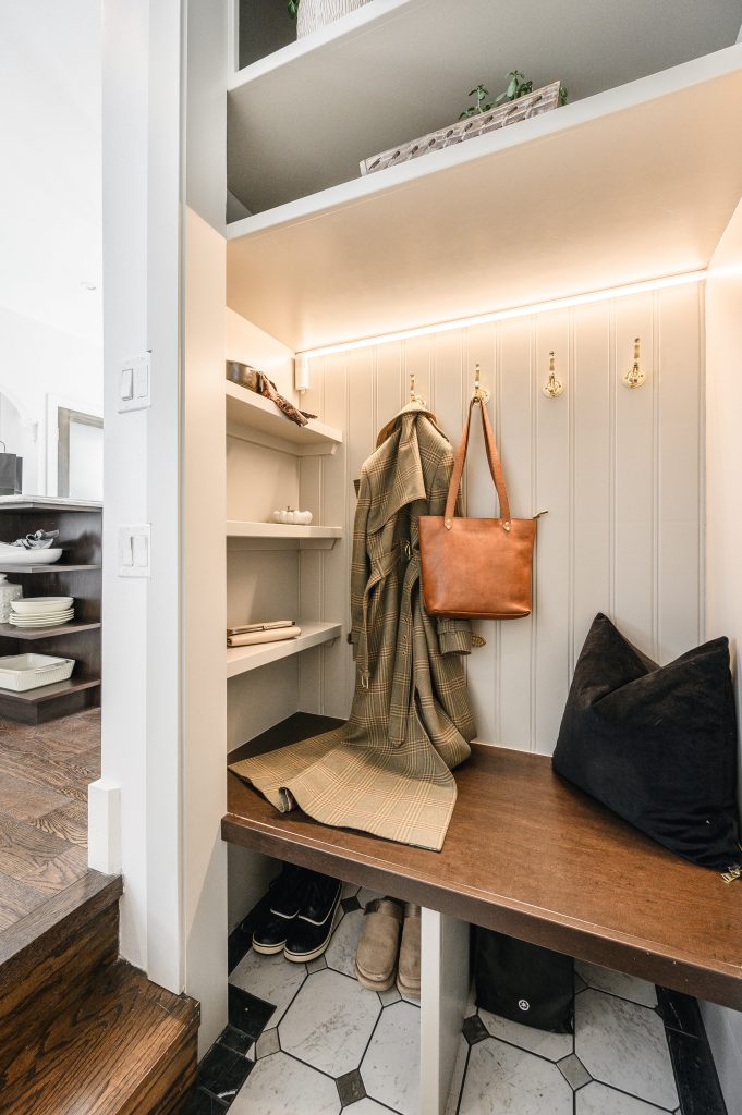 Built-in mudroom with open shelving, brass coat hooks, a bench, and warm LED strip lighting for a welcoming mudroom.