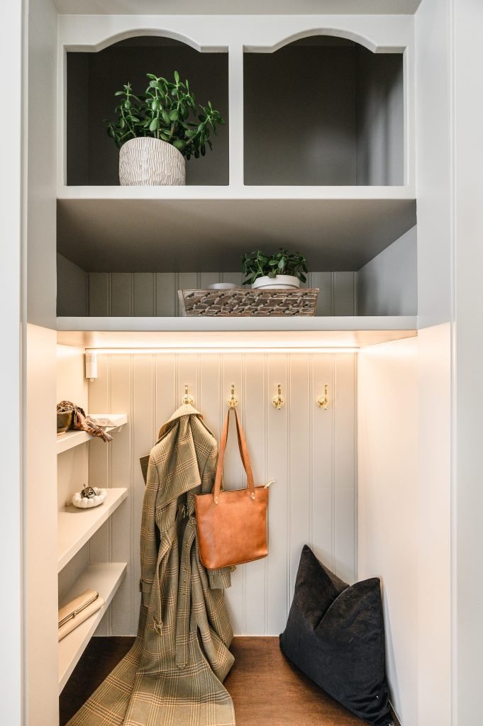 Mudroom built-in featuring arched cubbies with greenery, brass coat hooks, shelving, and a leather tote hanging below.