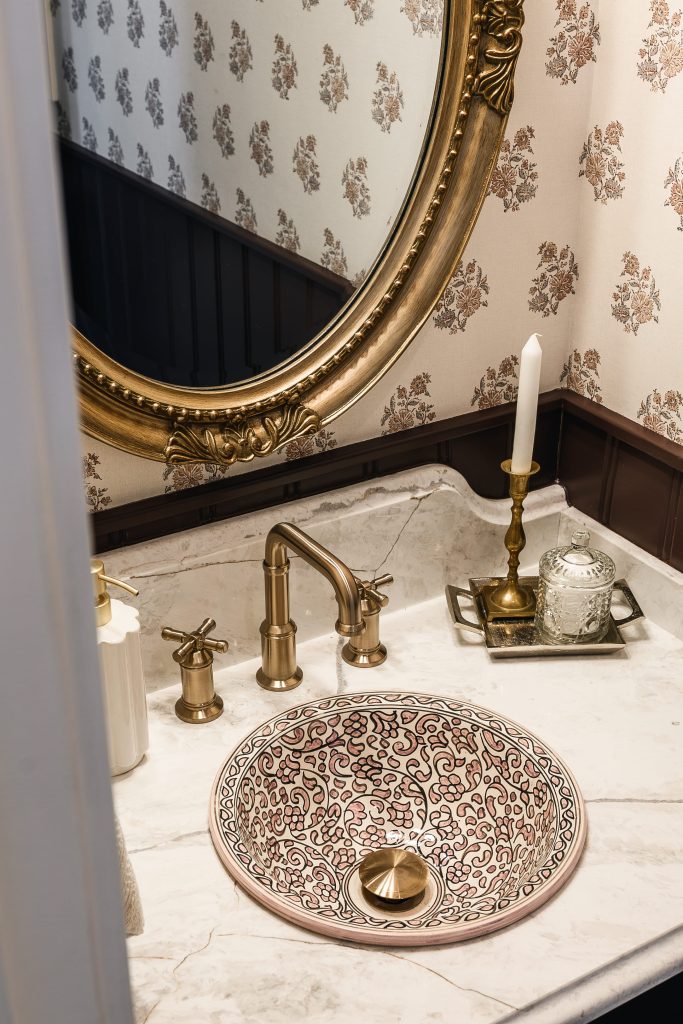 Close-up of a patterned sink with antique brass cross-handle faucet, candle, and marble countertop.