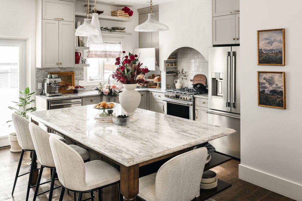 Victorian-inspired kitchen island with a marble countertop and dark wood base surrounded by cream upholstered bar stools.