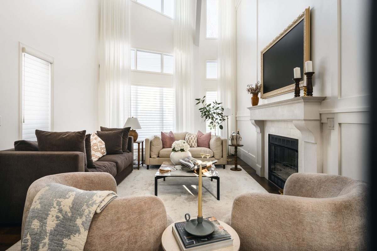 Double-height Victorian-inspired living room with a neutral sofa grouping, white tiled fireplace, and full-length sheer drapes.