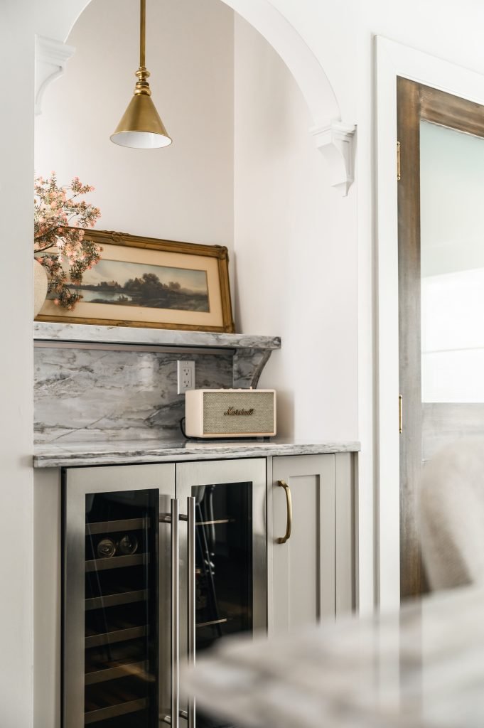 Close-up of the built-in arched wine bar with marble countertop, a Marshall speaker, brass pendant, and wine refrigerator.