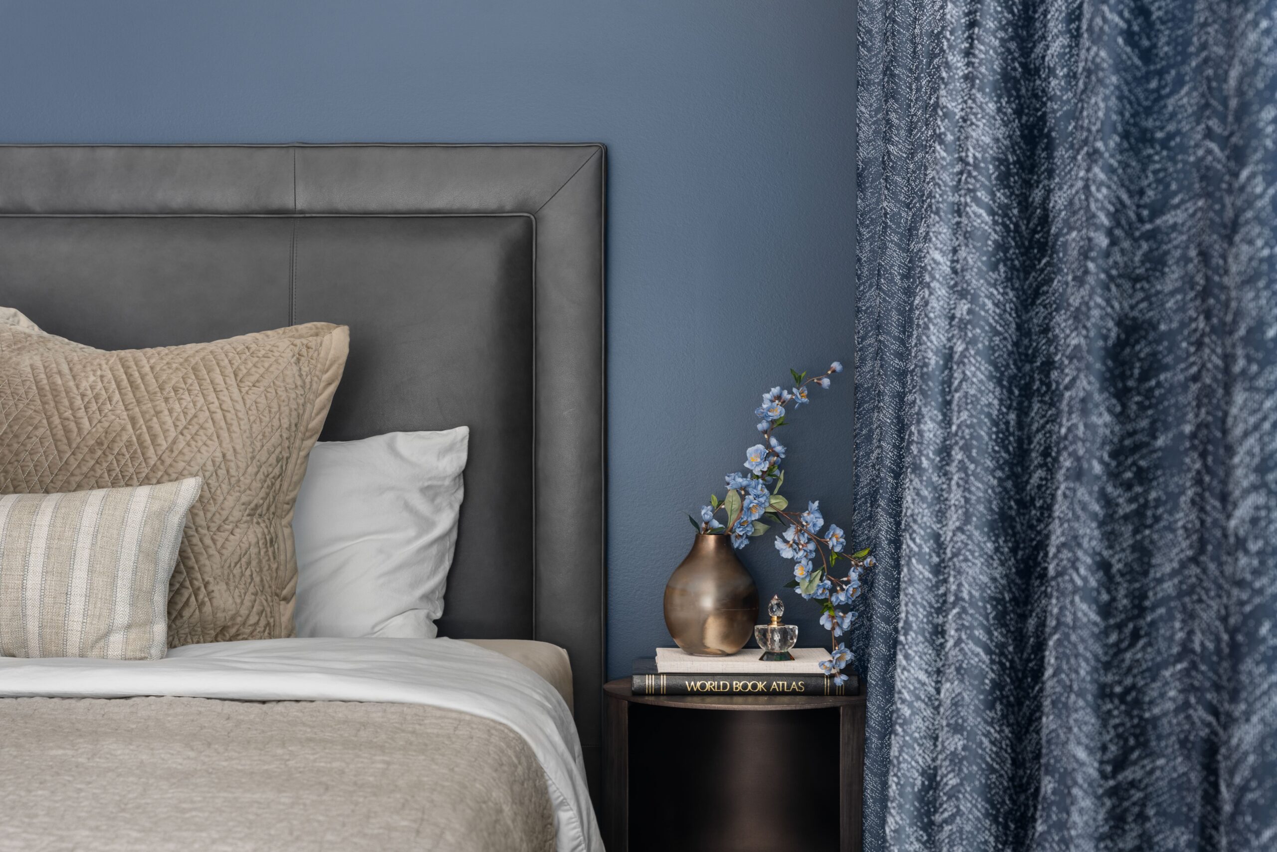 Close-up of bedside styling with blue blossoms in a bronze-toned vase, stacked books and a small decorative bottle on the nightstand.