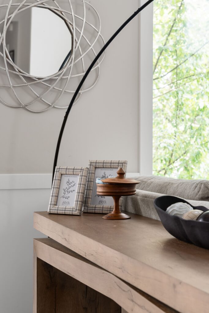 A console table vignette, decorated with framed photos, a lidded wooden dish, and a decorative bowl.