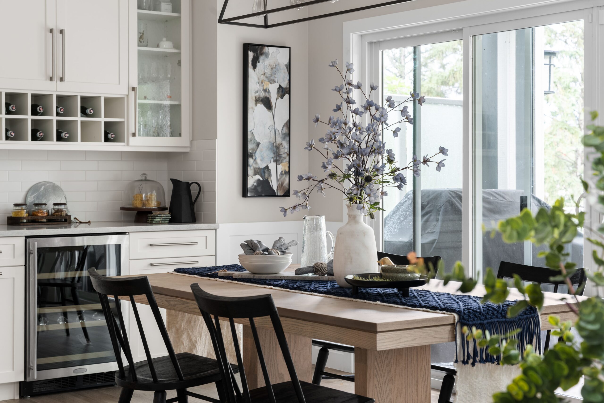 The dining table is styled with a ceramic vase, dark blue table runner, and place settings beneath a linear pendant light.