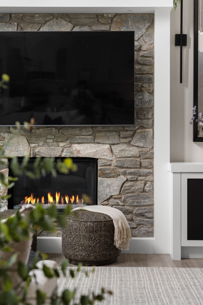 A close view of the fireplace with TV mounted above. A pouf with a throw blanket on top of it sits in front.