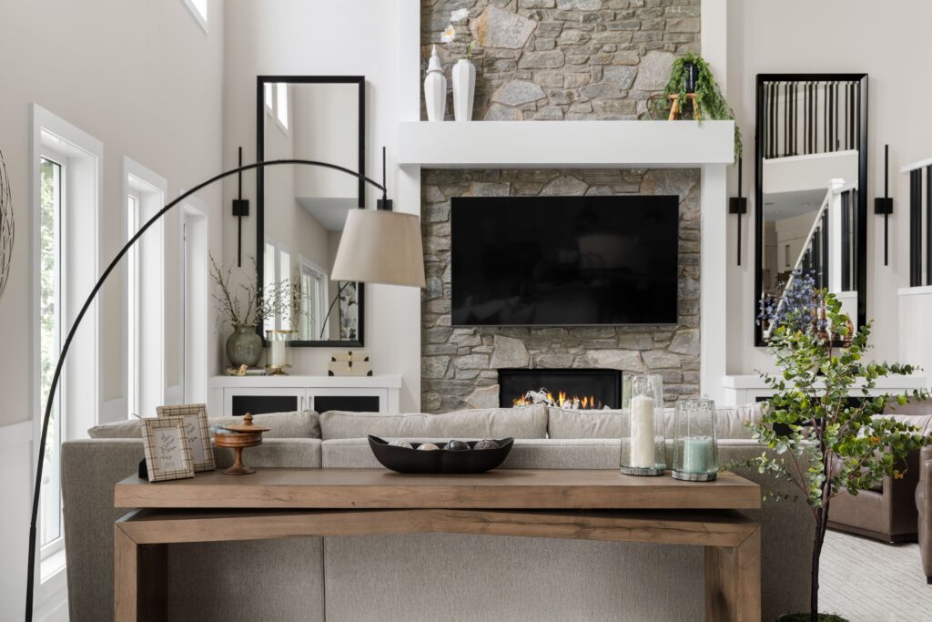 A wide view of the living room, its light wood console table styled with framed photos and candle holders, the stone fireplace in the background.