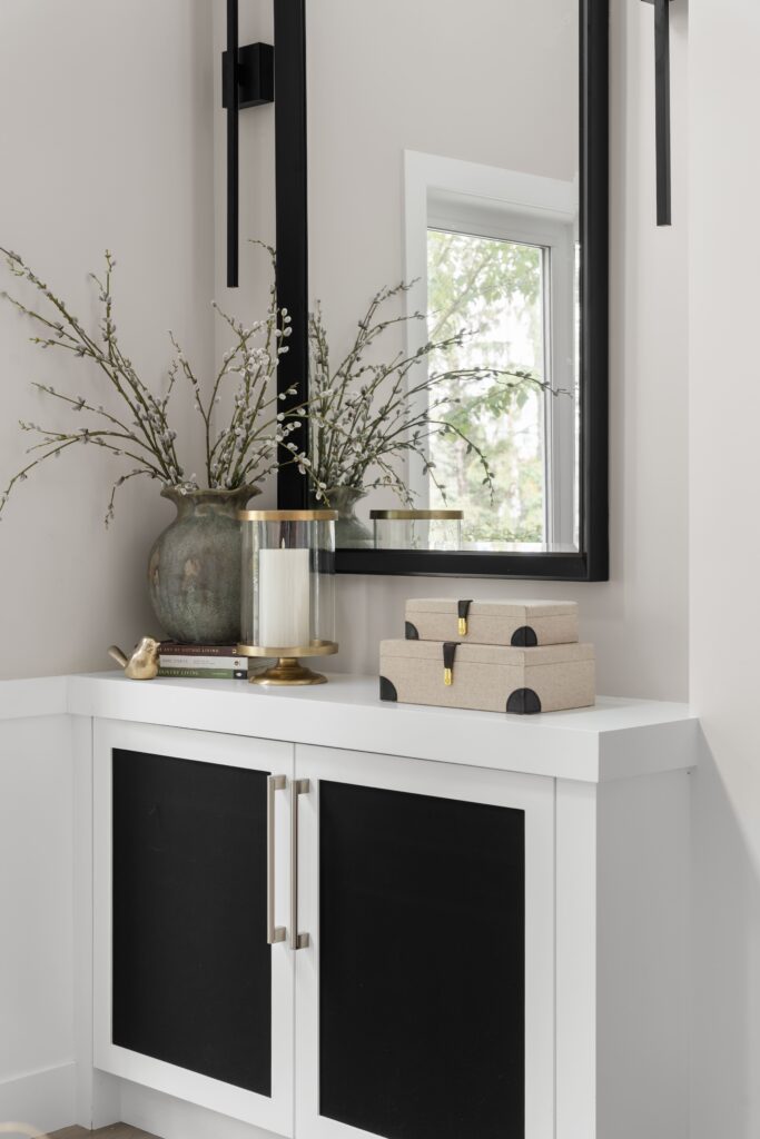 A console vignette with a vase of willow branches, a glass candle holder, and stacked fabric storage boxes.