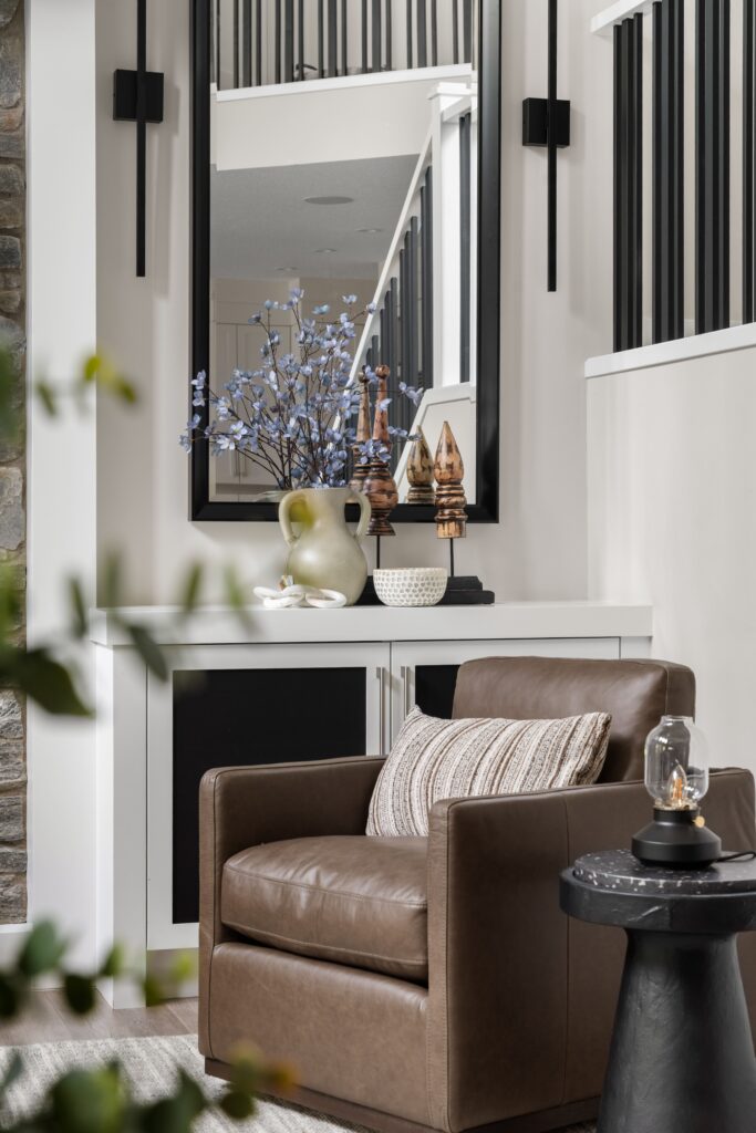 An armchair paired with a black circular side table and lantern-style lamp, set beneath a mirror reflecting the staircase.
