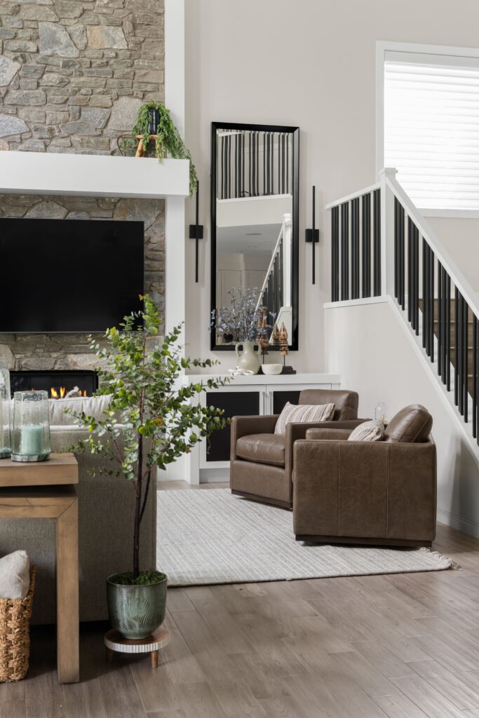 A pair of leather swivel armchairs sit near the staircase, with a built-in cabinet and mirror rounding out this family room corner.