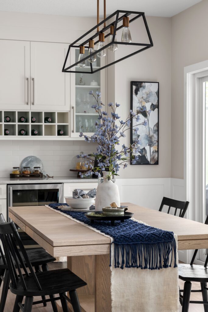 The dining area sits beside a wine bar with glass-front cabinetry, the table decorated with a navy woven table runner and blue florals.