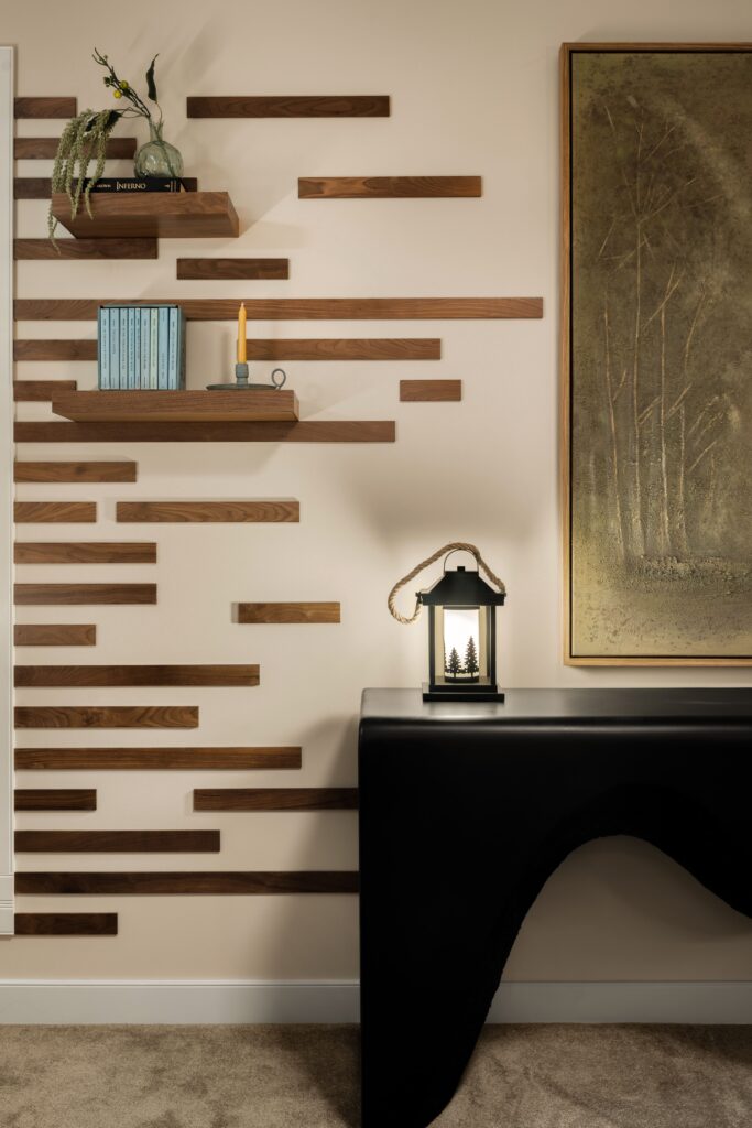 A wood slat accent wall with floating shelves, styled with books and a candle beside a black console table.