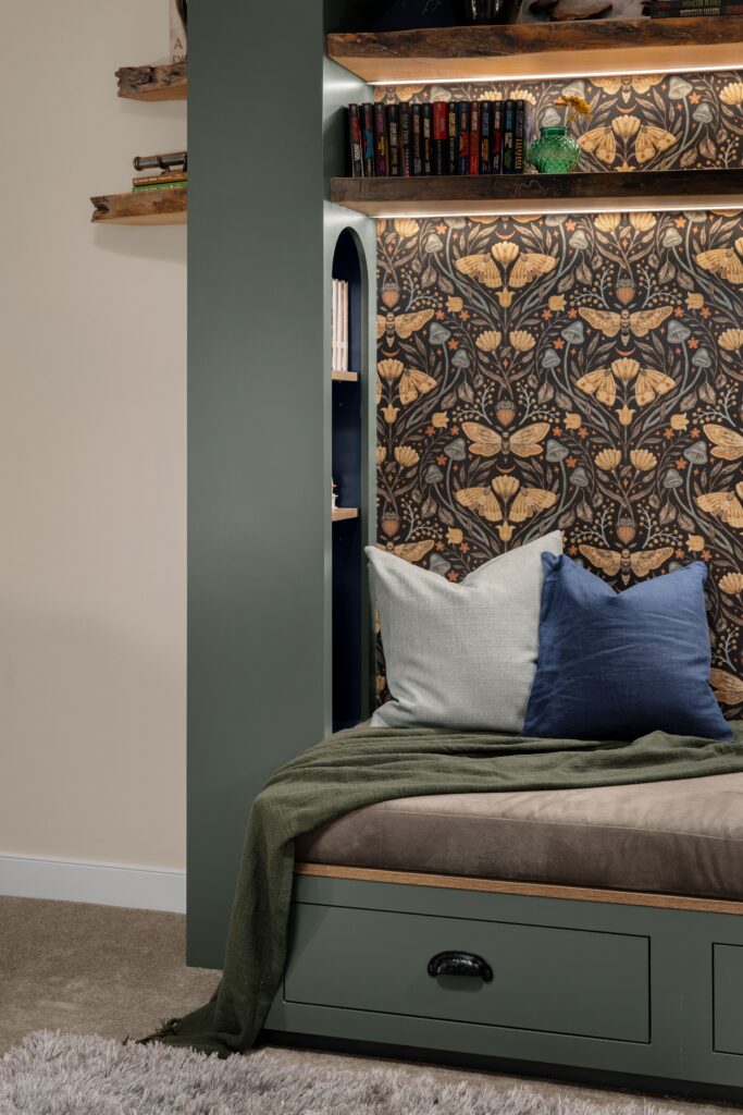 A cozy nook corner complete with a dark green throw blanket, fluffy pillows, and a hidden section of the built-in bookshelf.