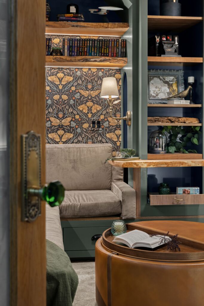 A view through the door, complete with a glass doorknob, into the cozy reading nook with a custom-upholstered loveseat and gold wall sconce.