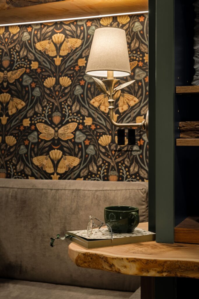 A brass wall sconce mounted on the built-in shelving, above the live-edge desk which is holding a book, a coffee mug, and reading glasses.